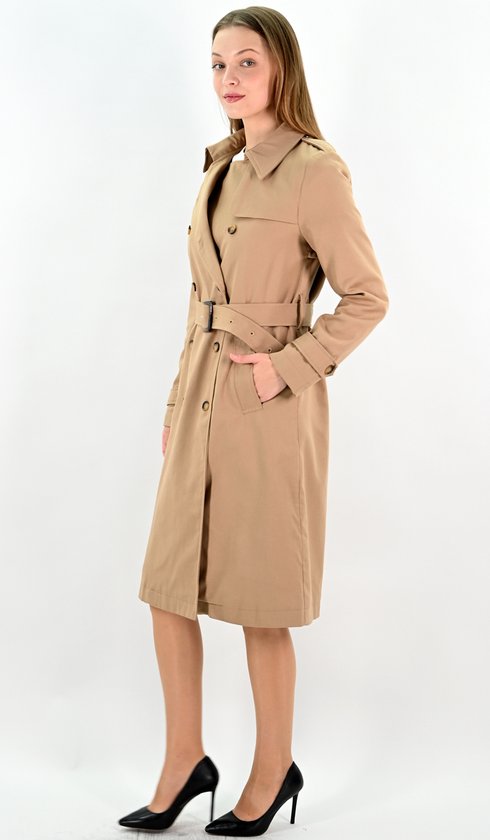 Model in camelkleurige lange trenchcoat met ceintuur, rechterhand in de zak.