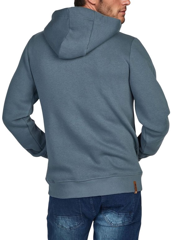 Achterkant van een man in een blauwgrijze hoodie met rits, spijkerbroek en handen in de kangoeroezakken.