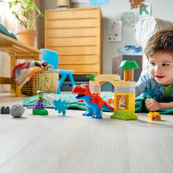 Een jongetje speelt met LEGO Duplo blokken, waaronder een rode en blauwe dinosaurus, groene goblin en een fort.