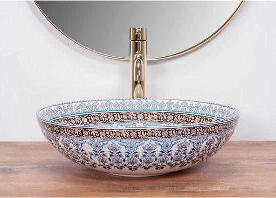 Keramische wastafel met Delfts blauw patroon en gouden kraan op een houten meubel, met spiegel.