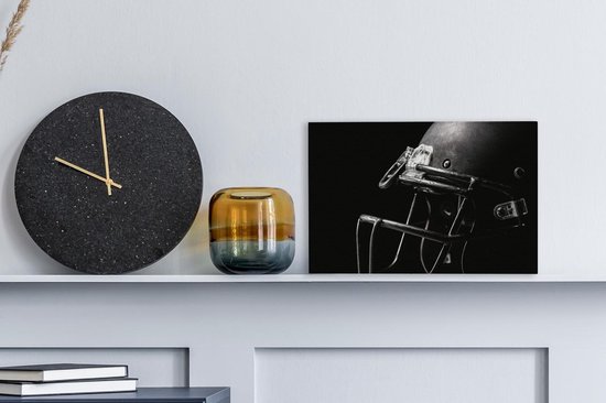 Un casque de football américain noir avec masque, à côté d'une horloge ronde et d'un vase sur une étagère.
