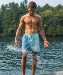 Man met gespierd bovenlichaam die water spettert, draagt een blauwe zwembroek die aan de linkerkant donkerder is.