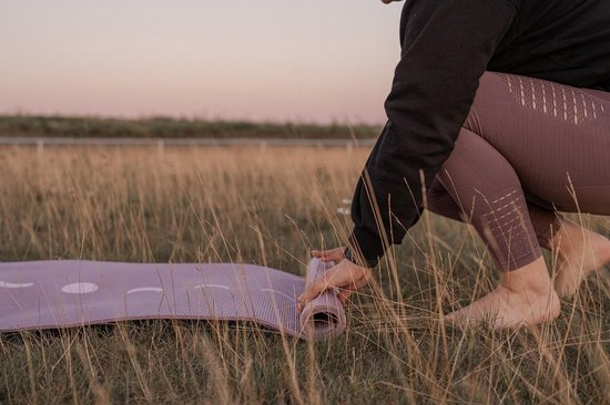 Een vrouw rolt een lavendelpaarse yogamat uit in het gras.