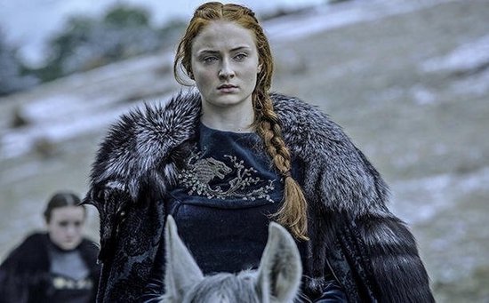 Sansa Stark met gevlochten rood haar, draagt een donker fluwelen jurk met bontkraag.