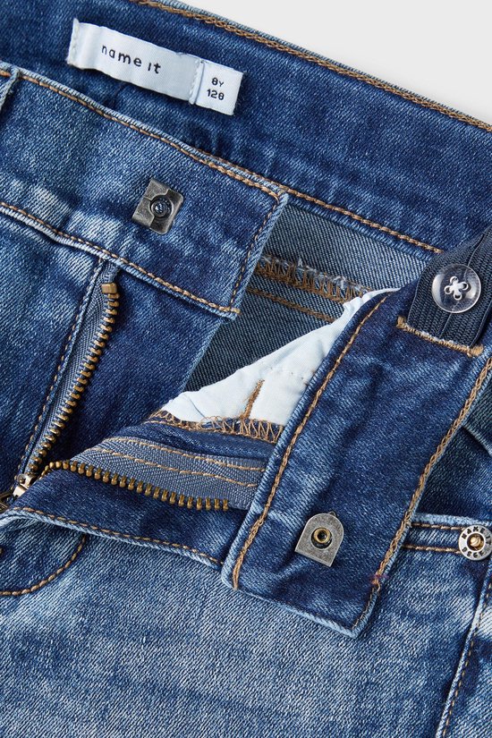 Detail van de gulp van een blauwe spijkerbroek met rits en knopen.