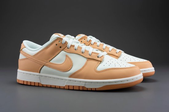 Een paar Nike Dunk Low damesschoenen, wit met oranje overlays, op een grijze achtergrond.