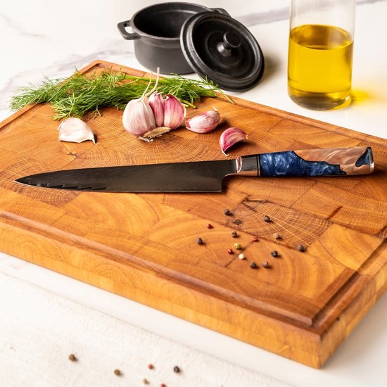 Een Japans koksmes met blauw en beige handvat ligt op een houten snijplank met knoflook en dille.