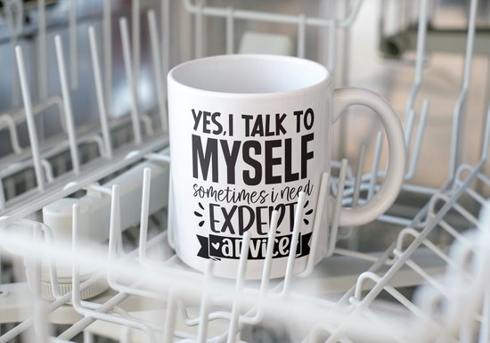 Witte mok met tekst "YES, I TALK TO MYSELF SOMETIMES I NEED EXPERT ADVICE" in een vaatwasser.