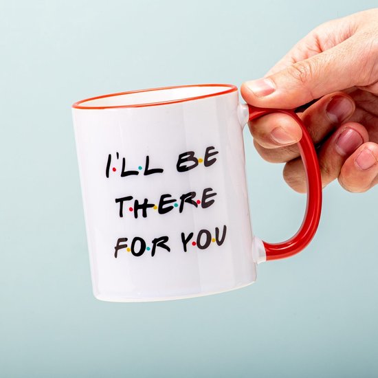 Hand houdt witte mok vast met rode rand en tekst I'LL BE THERE FOR YOU met gekleurde stippen tussen de letters.