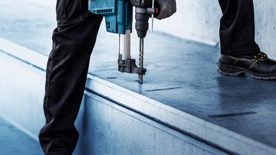Bosch boorhamer met stofafzuiging boort in een betonnen structuur.