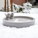Grijze vogeldrinkschaal met decoratieve vogels, geplaatst in een besneeuwd winterlandschap.