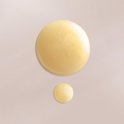Twee druppels goudkleurig, glanzend serum op een lichtbeige achtergrond.