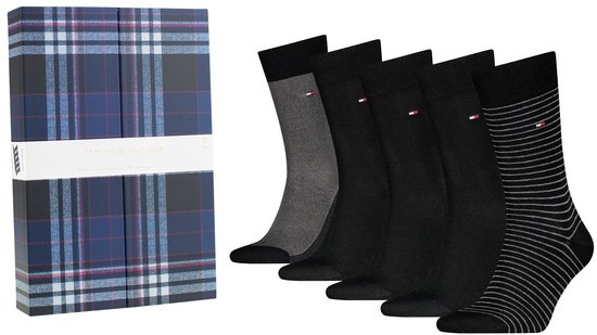 Een geschenkverpakking met een blauw ruitpatroon en het Tommy Hilfiger logo, naast vijf paar Tommy Hilfiger sokken: één grijs, drie zwart, één met grijze strepen.