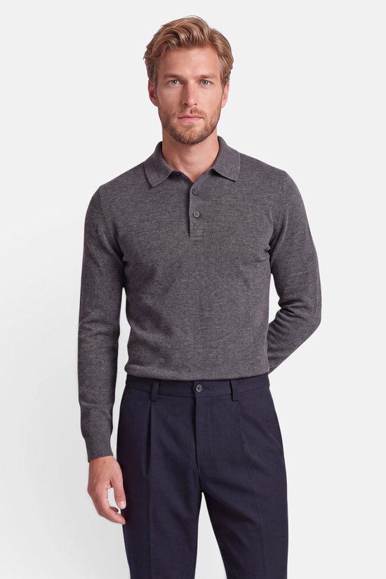Man met blond haar in een donkergrijze polotrui met lange mouwen en een donkere pantalon.