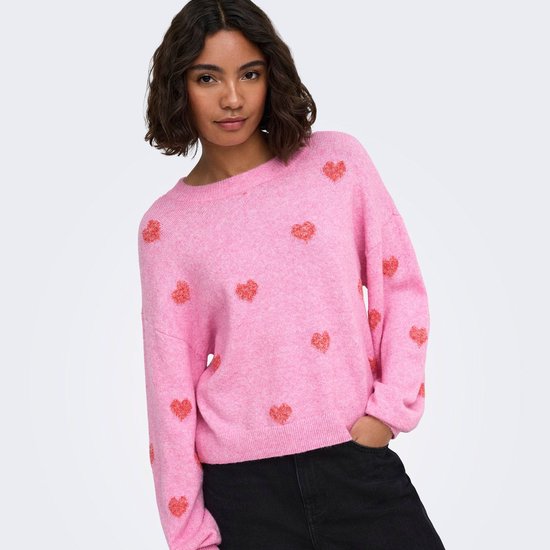 Model draagt een roze trui met lange mouwen en een all-over print van kleine rode hartjes.