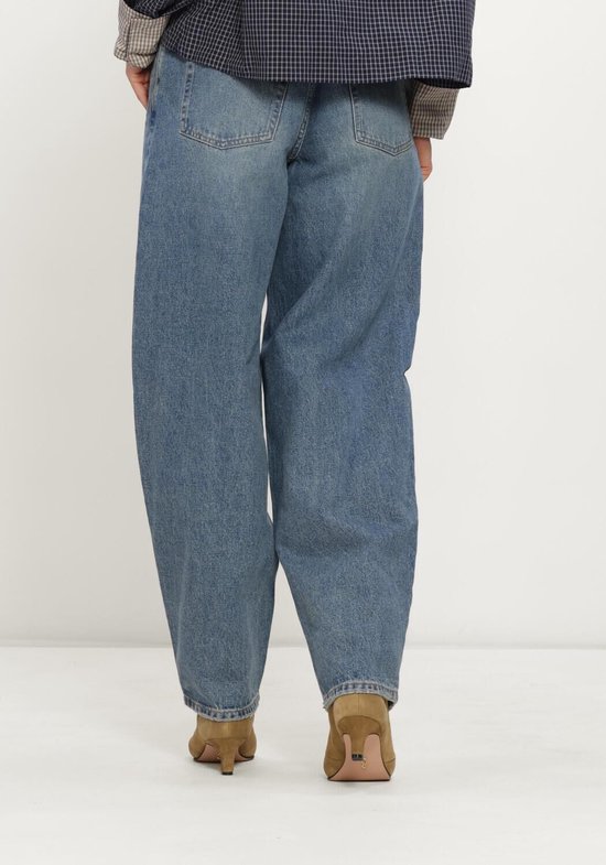 Een model van achteren gezien, draagt een blauwe spijkerbroek met wijde pijpen en bruine schoenen.