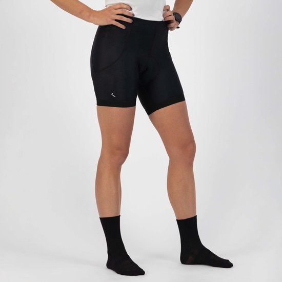 Vrouw met handen in de zij, draagt een zwarte fietsbroek en zwarte sokken. Zilverkleurig logo zichtbaar op linkerpijp.