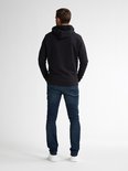 Model van achteren met zwarte hoodie en donkerblauwe slim fit jeans op witte achtergrond.