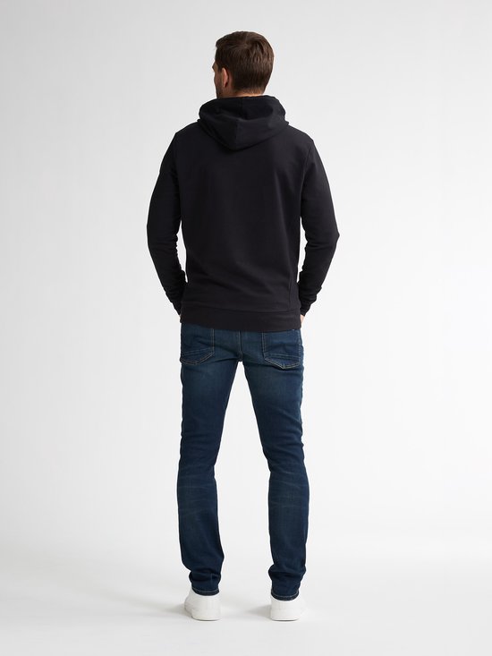 Model van achteren met zwarte hoodie en donkerblauwe slim fit jeans op witte achtergrond.