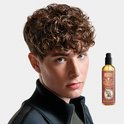Jonge man met bruin krullend haar naast een fles Reuzel Spray Grooming Tonic.