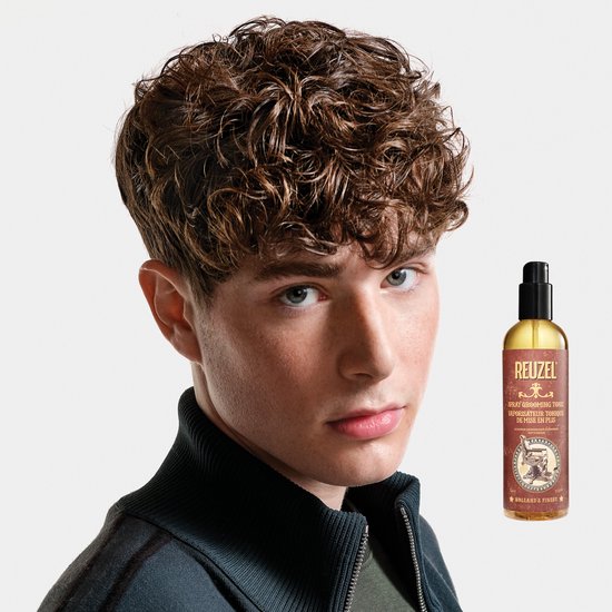 Jonge man met bruin krullend haar naast een fles Reuzel Spray Grooming Tonic.