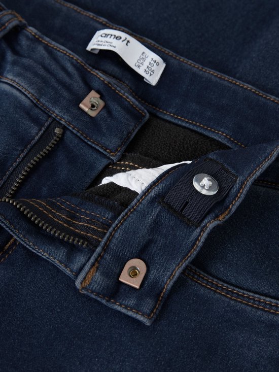 Close-up van de sluiting van een donkerblauwe jeans met 'name it' label, rits en verstelbare tailleband.