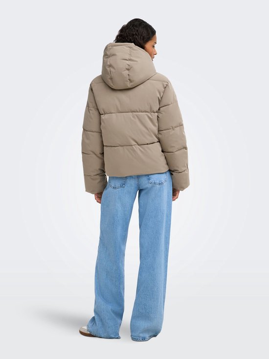 Model van achteren gezien in een beige pufferjas en wijde jeans, staand tegen een neutrale achtergrond.