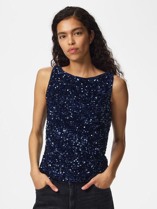 Een vrouw met lang krullend haar draagt een donkerblauw mouwloos topje met pailletten en een zwarte jeans.