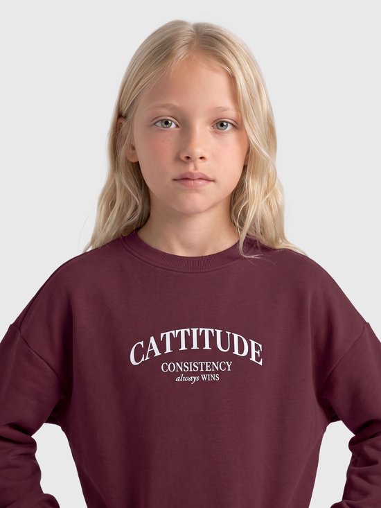 Meisje in bordeauxrode trui met 'CATTITUDE CONSISTENCY always WINS' opdruk.