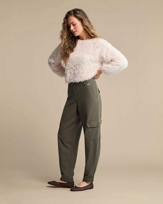 Model met lang golvend haar draagt een pluizige ecru trui met lange mouwen en een legergroene cargo broek.