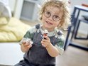Glimlachend kind met bril houdt een Duplo brandweerman en een wit katje vast.