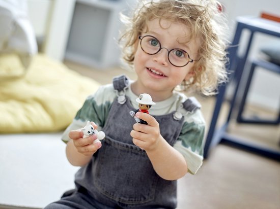 Glimlachend kind met bril houdt een Duplo brandweerman en een wit katje vast.