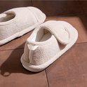 Beige pluche pantoffels met een verstelbare klittenbandsluiting en een wit treklipje bij de hiel.