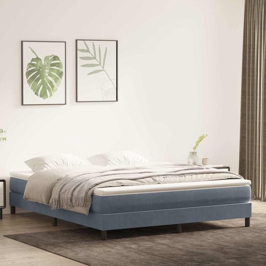 Blauw fluwelen boxspringbed met witte matras, grijze deken en zwarte poten in een moderne slaapkamer.