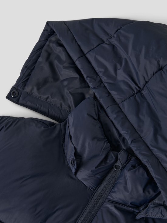 Detail van de capuchon en ritssluiting van een donkerblauwe, gewatteerde jas.