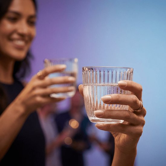 Une femme tient un verre côtelé rempli d'eau. L'arrière-plan a une ambiance festive.