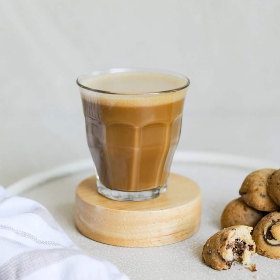 Un verre Duralex transparent avec cannelures verticales, rempli de café, sur une rondelle de bois.