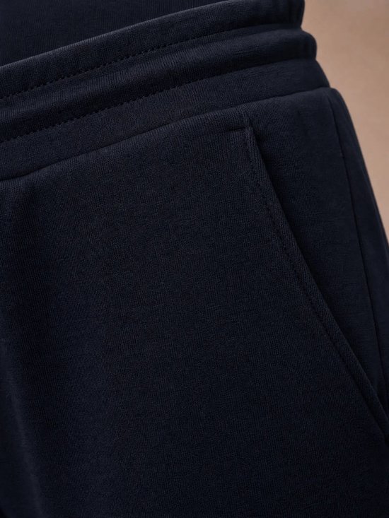 Detail van de zak van een donkerblauwe sportbroek met witte stiksels.