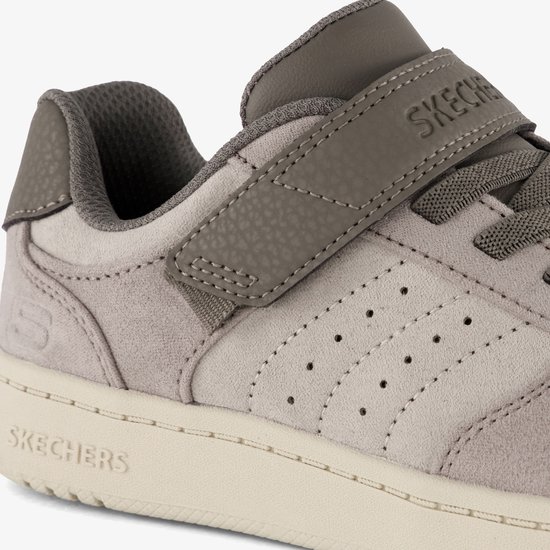 Close-up van een taupe Skechers sneaker met suède en leren details, een klittenbandsluiting en perforaties.