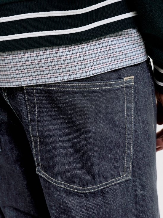 Close-up van de achterzak van een donkere jeans met contrasterende stiksels.