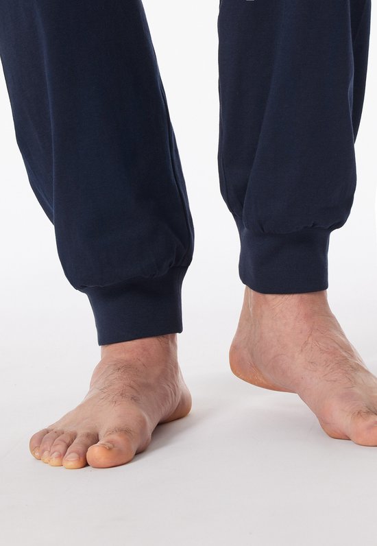 Voeten van een man in donkerblauwe pyjamabroek met elastische enkels.