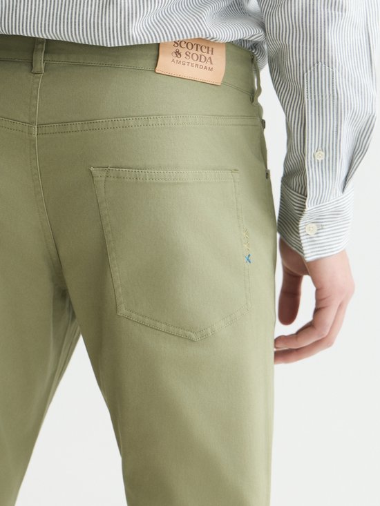 Detail van de achterkant van een olijfgroene chino met leren logo patch.