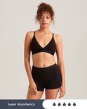 Model met krullend haar in zwarte Slaapshort en zwarte bralette. Tekst zegt 'Super Absorbency'.
