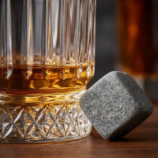 Een whiskeysteen ligt op de geprinte onderkant van een gegroefd glas met amberkleurige whiskey.