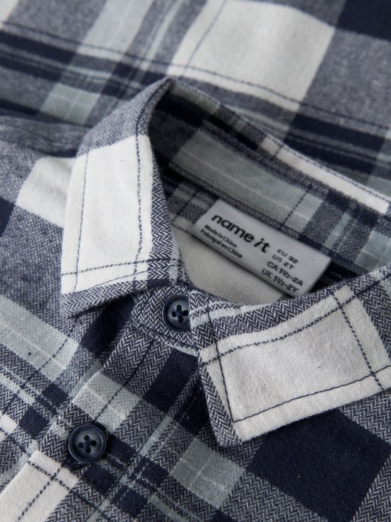Detailopname van de kraag en het label van het blauw-wit geruite overhemd.