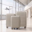 Drie beige koffers in een luchthaven, met een vliegtuig op de achtergrond.
