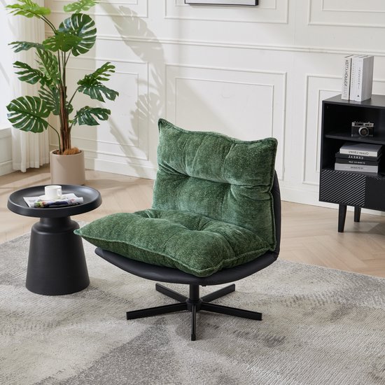 Groene fauteuil met zachte, getufte kussens en een zwart lederen zitting, in een woonkamer met plant en bijzettafel.