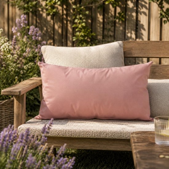 Coussin décoratif rose de 30 x 50 cm sur un banc de jardin en bois avec d'autres coussins et de la lavande.