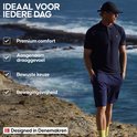 Man in donkerblauw poloshirt en korte broek, staand op een rotsachtige kust met de zee op de achtergrond.