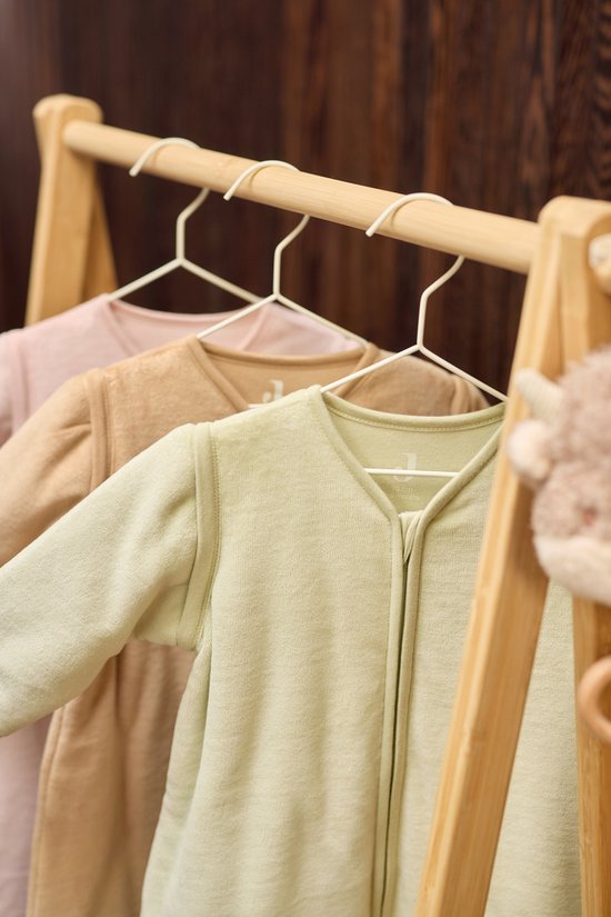 Drie baby slaapzakken in pastelkleuren: lichtroze, beige en mintgroen, hangend aan een houten rek.